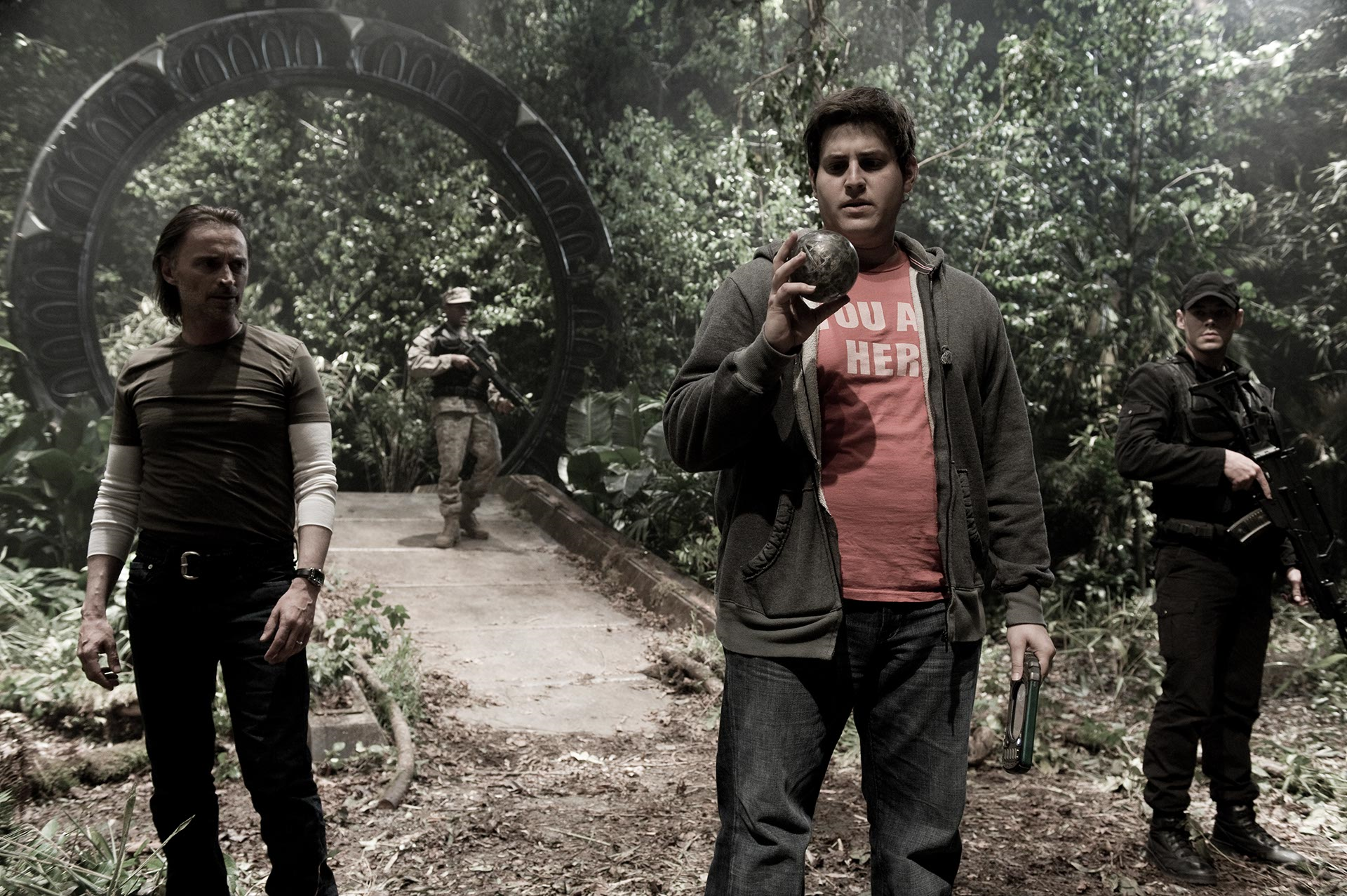 Stargate Universe characters standing in a forest with the Stargate behind them.